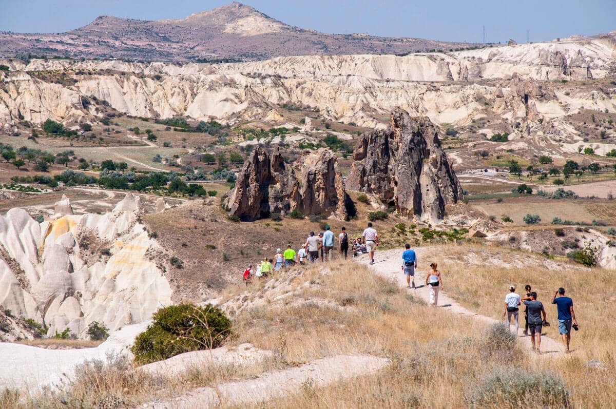 Walkers on a ridge trail through a valley of fairy chimneys and eroded rock, a mountain on the horizon