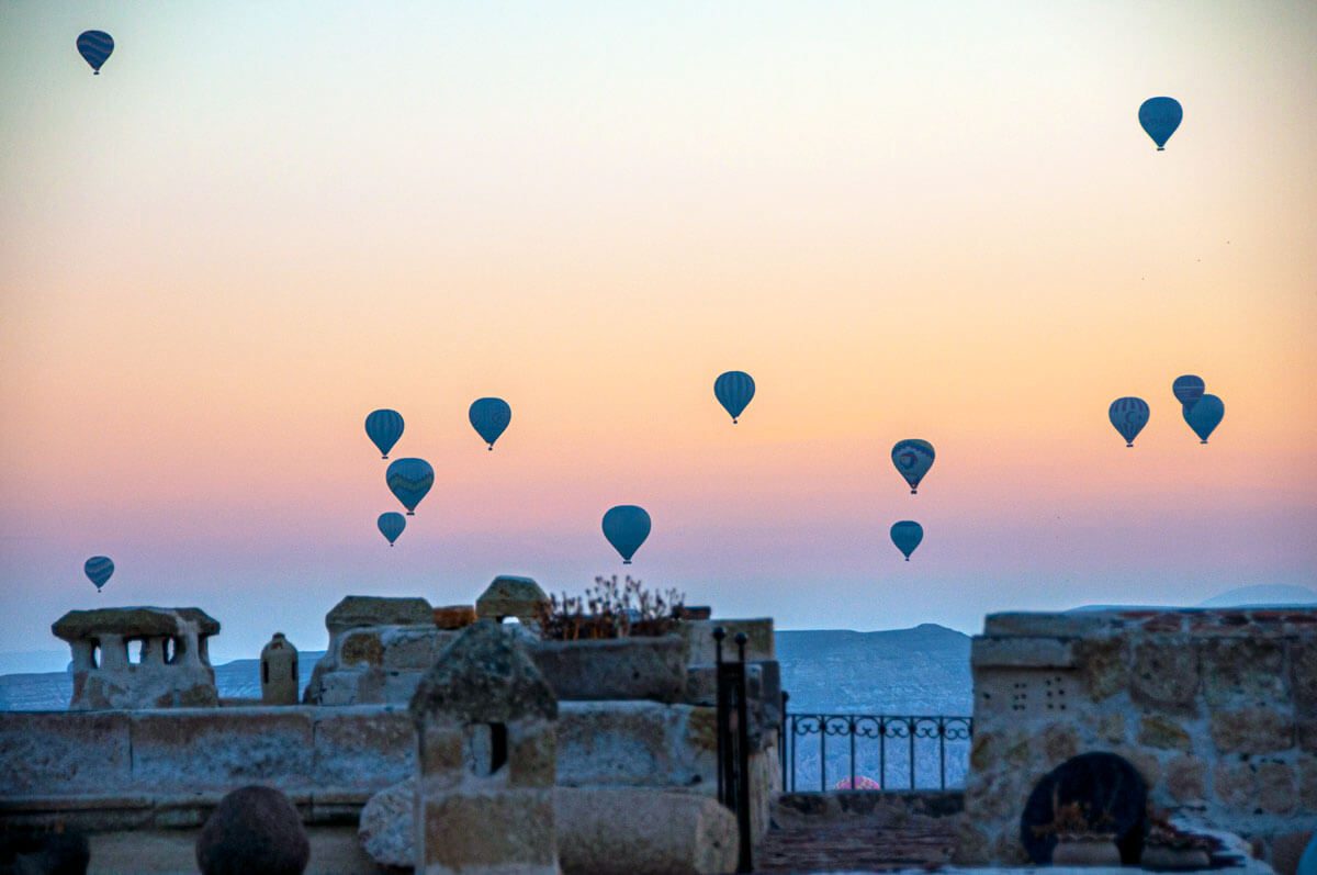 Hot air balloons drifting past a stone rooftop terrace at first light