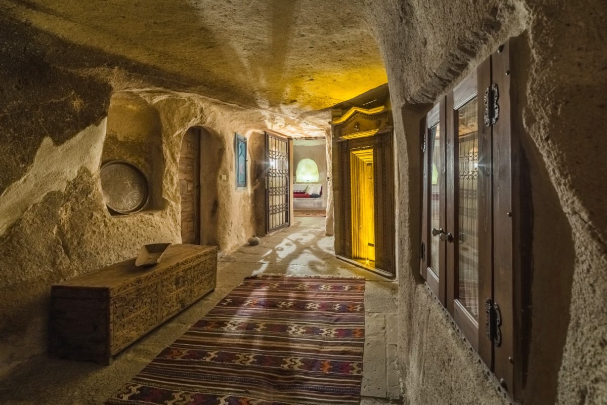 A stone-carved corridor inside a cave hotel, a kilim runner underfoot and carved wooden doors along the walls