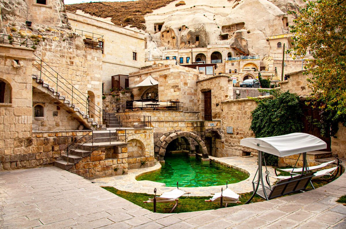 A cave hotel courtyard with a stone-carved plunge pool and terraces climbing the rock behind it