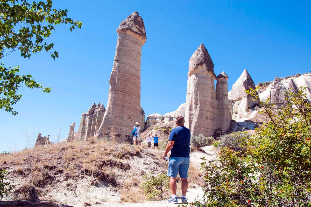 Visitors beneath the tall rock pillars of Love Valley, their caps still balanced after centuries of erosion