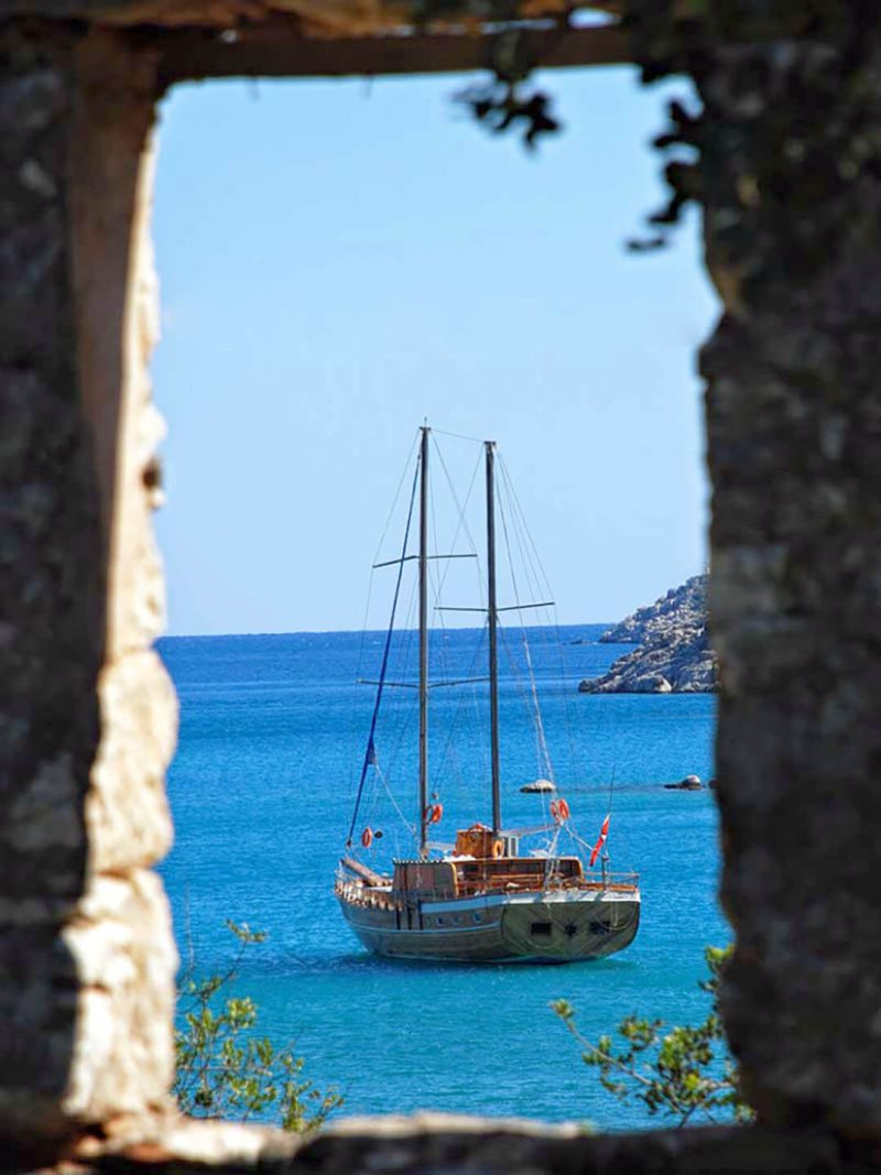 A gulet at anchor in a turquoise bay, framed by an old stone window.